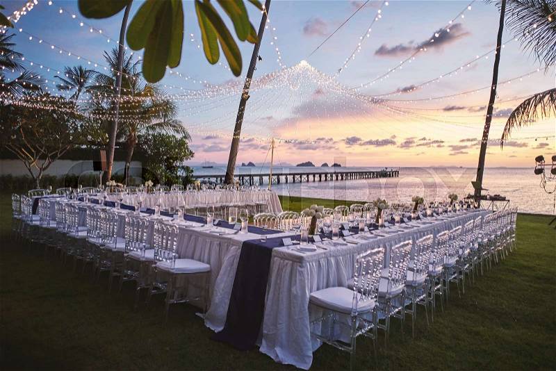 Beach wedding reception dinner venue arrangement at sunset with orange sky decoration with light strips, stock photo