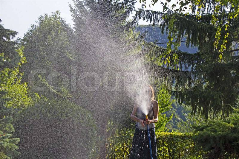 A young woman Watering a lawn in the yard of the house, a background sunlight, stock photo