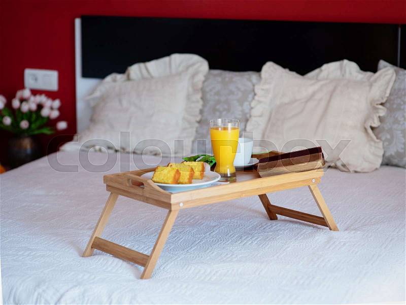 Breakfast served in bed on a wooden tray with tea, juice, cookies. Hotel room service, relax concept, stock photo