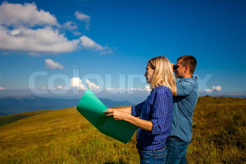 The good pair with binocular and a map are looking for a road in the mountains, stock photo