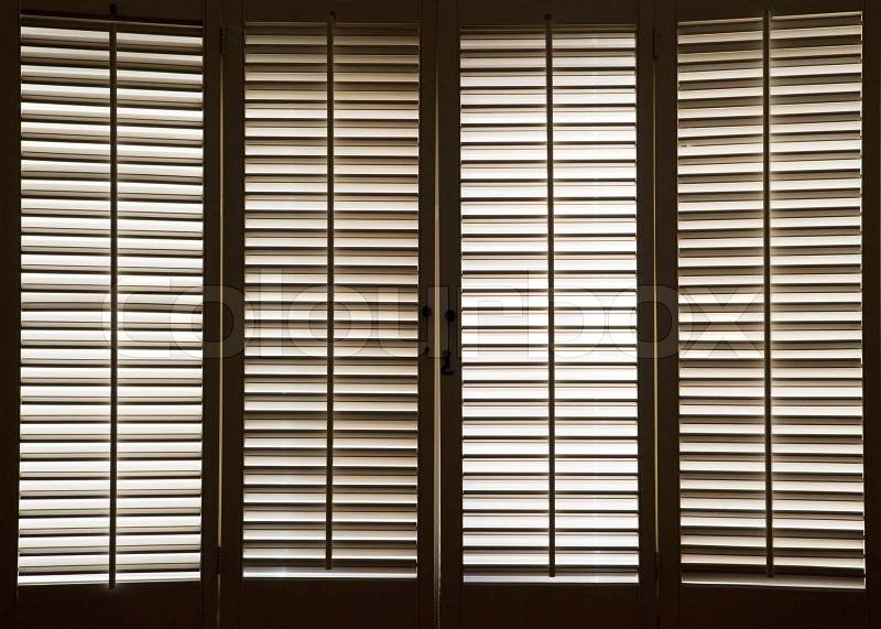 Wooden shutters in front of bright, sunlit windows, stock photo