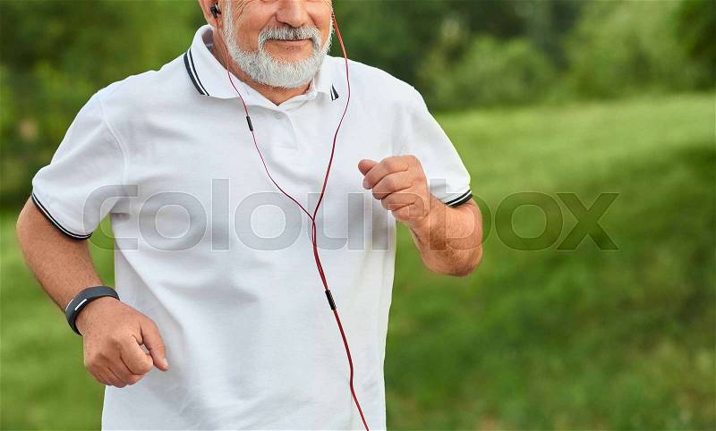 Cropped frontview of running old man having white beard. Wearing classic white polo shirt with dark blue stripes, sport watch and red headphones. Looking sporty, ..., stock photo
