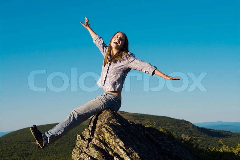Happy woman on top of the wold sitting on the rock and scream with hands up, stock photo