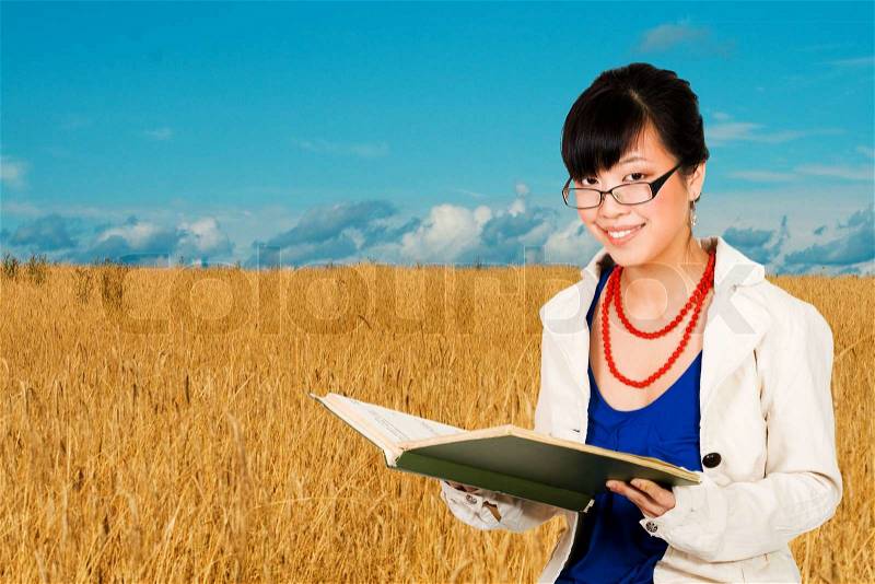 Asian woman with a book in wheat field - agriculture specialist, stock photo