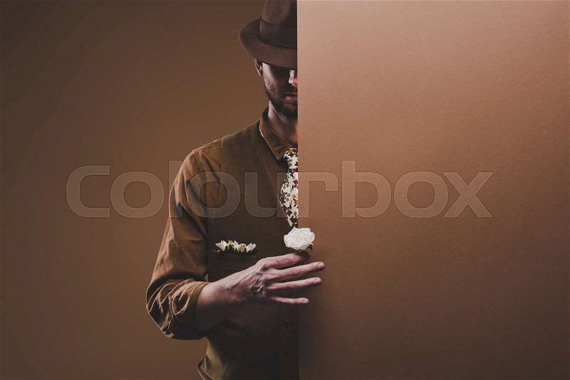 Man in stylish clothes holding rose flower isolated on brown, stock photo
