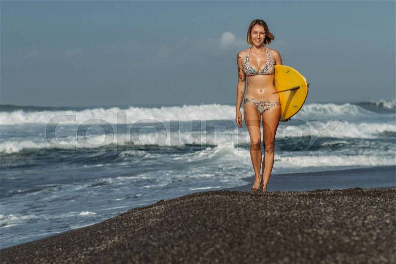 Beautiful girl in swimsuit walking on beach with surf board, stock photo