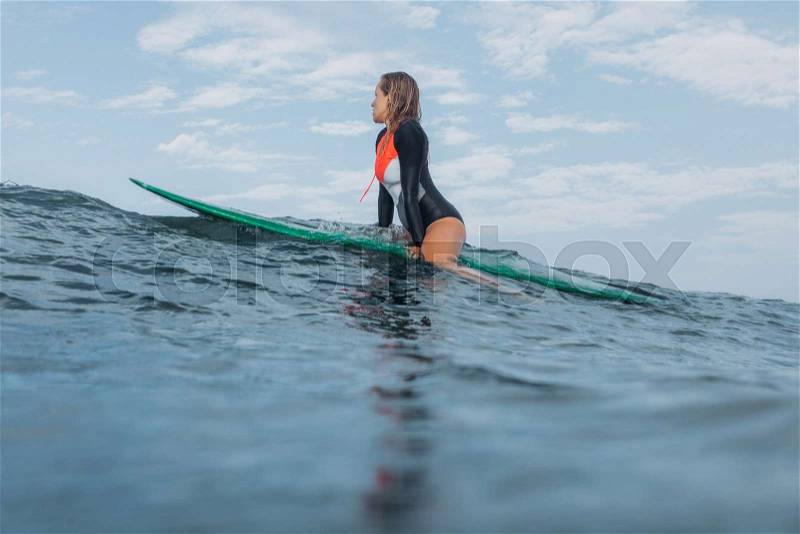 Female surfer sitting on surf board in ocean, stock photo