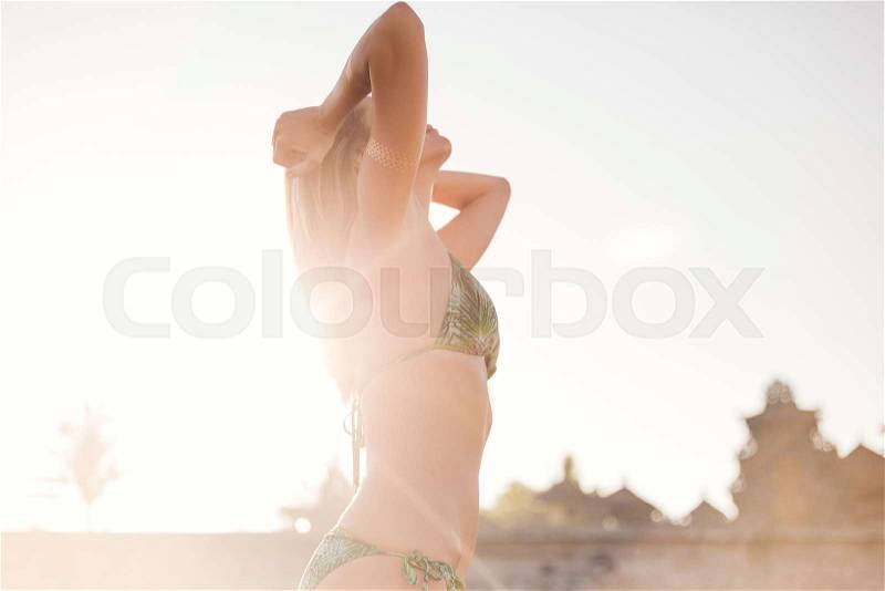 Side view of beautiful young woman in bikini playing with hair with sunlight on background, stock photo