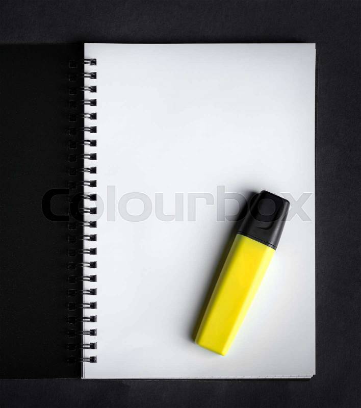 Black spiral notebook with yellow marker on the black paper background, stock photo
