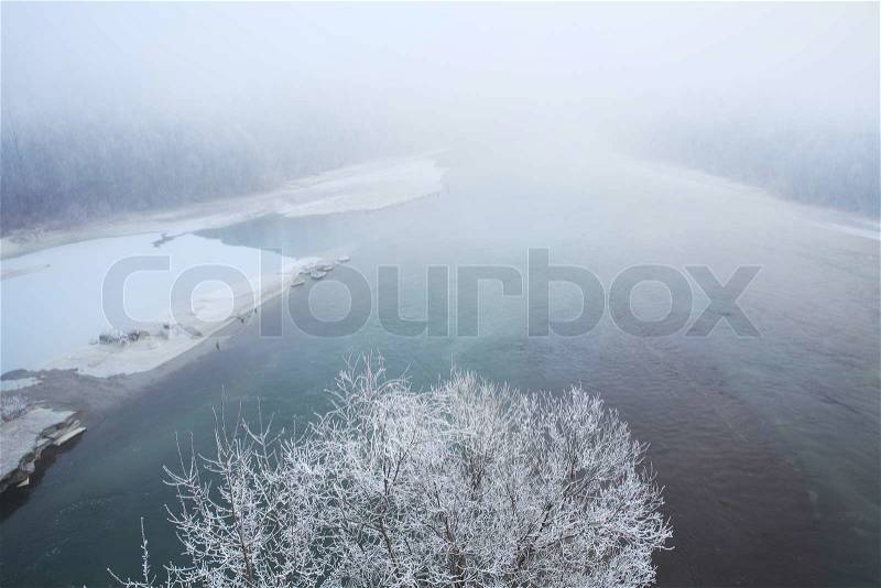 Rime frost on trees and thin ice on Tanaro river at hazy day in Piedmont, Northern Italy, stock photo