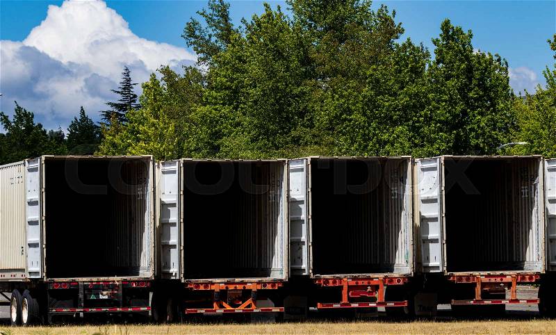 Semi tractor trailers empty and open parked in a lot with trees and brown grass, stock photo
