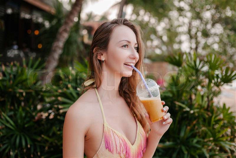 Smiling attractive girl in bikini top drinking cocktail, stock photo
