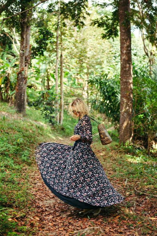 Woman spinning around in dress on path in jungle, stock photo