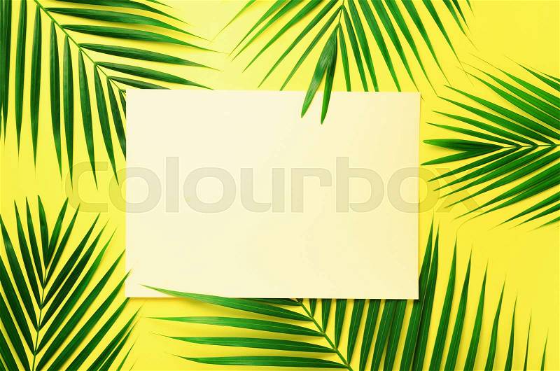Tropical palm leaves on pastel yellow background with paper card note. Minimal summer concept. Creative layout. Top view, flat lay. Green leaf on punchy pastel ..., stock photo