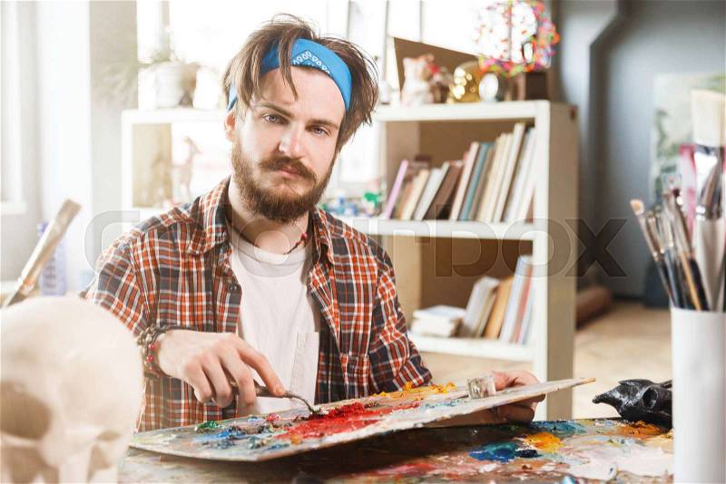 Portrait of a young bearded male artist is holding a brush and mix color oil painting on palette, stock photo