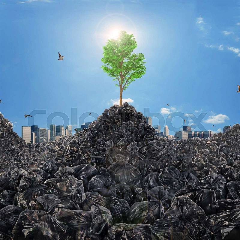 Concept of trash dump. Garbage dump in form of mountains with a growing tree on a city skyline background. Save the planet. Concept of recycle, stock photo