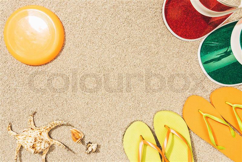 Flat lay with flying disk, colorful caps, flip flops and seashells on sand, stock photo