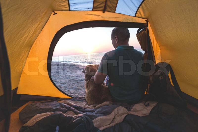 Happy weekend by the sea - man with a dog in a tent on the beach at dawn. Ukrainian landscape at the Sea of Azov, Ukraine , stock photo