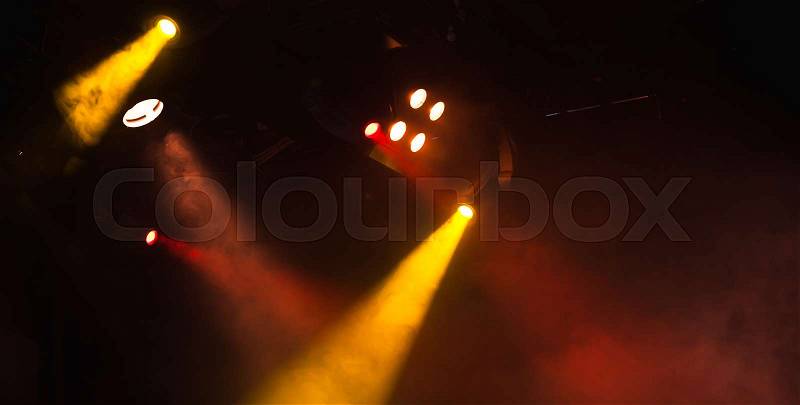 Red and yellow spot lights with strong beams in smoke over dark background, modern stage illumination equipment, stock photo