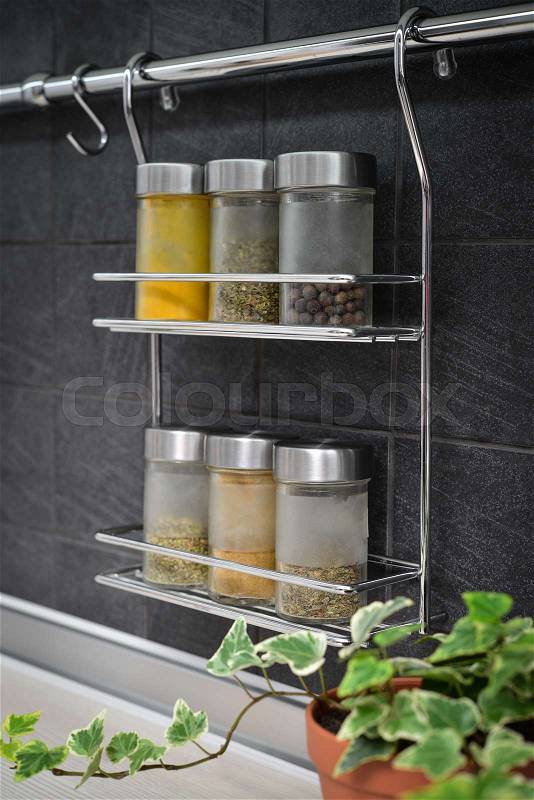 Jars of spices in hanging shelf in modern kitchen interior closeup, stock photo