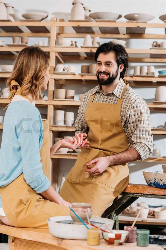Happy couple in aprons with ceramics and paints in pottery workshop, stock photo