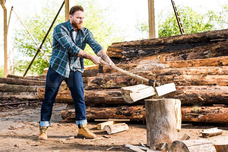 Lumberjack in checkered shirt chopping log at sawmill , stock photo