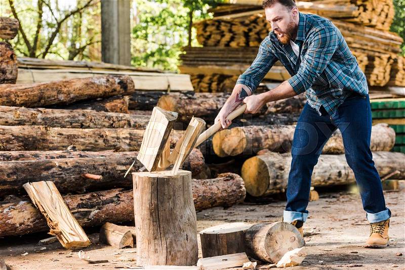 lumberjack in checkered shirt chopping log at sawmill , stock photo