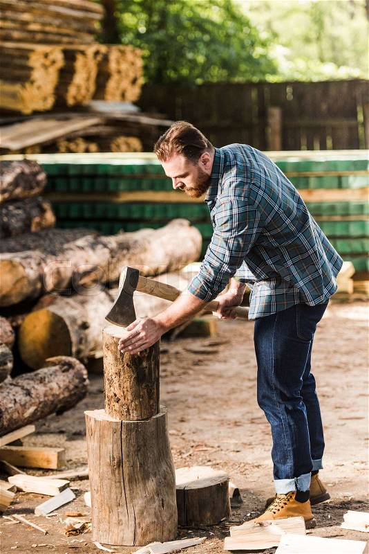 Lumberjack in checkered shirt chopping log at sawmill , stock photo
