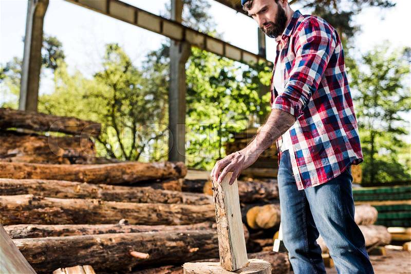 Lumberjack in checkered shirt preparing to chop half of log at sawmill , stock photo