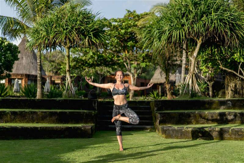 Happy woman in tree yoga pose with beautiful green plants on background, Bali, Indonesia, stock photo