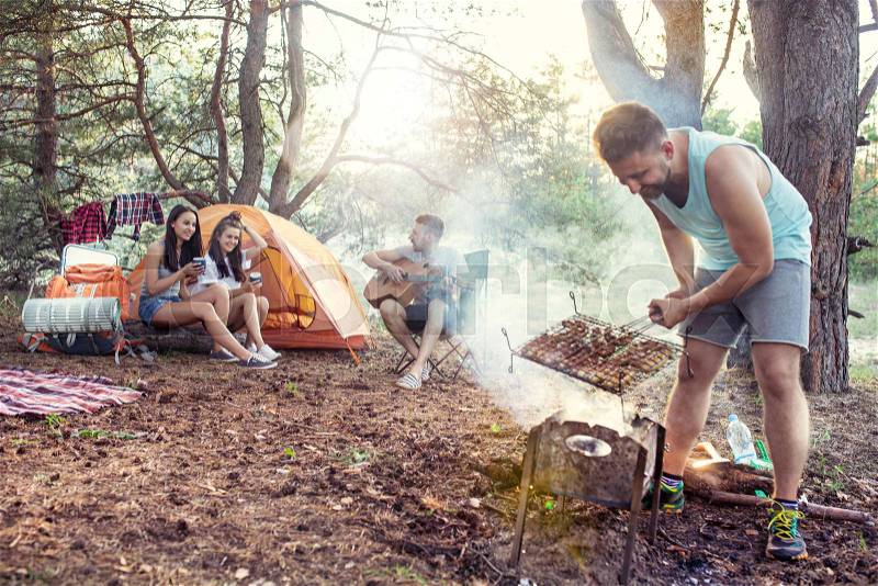 Party, camping of men and women group at forest. They relaxing, singing a song and cooking barbecue against green grass. The vacation, summer, adventure, lifestyle, picnic concept, stock photo