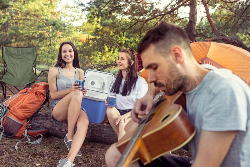 Party, camping of men and women group at forest. They relaxing, singing a song against green grass. The vacation, summer, adventure, lifestyle, picnic concept, stock photo