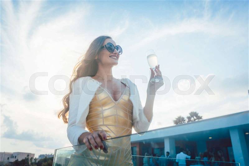 Woman having champagne at summer party with villa in the background, stock photo