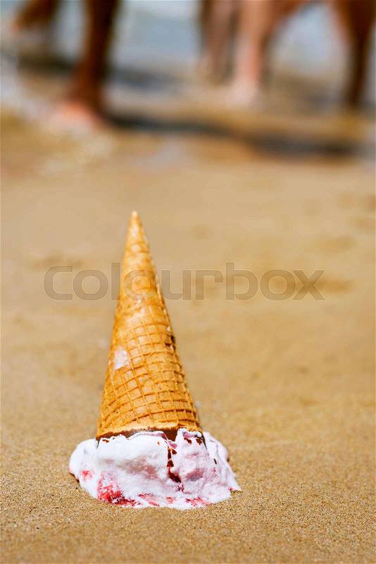 Closeup of an ice cream cone upside down dropped on the sand of a beach, stock photo