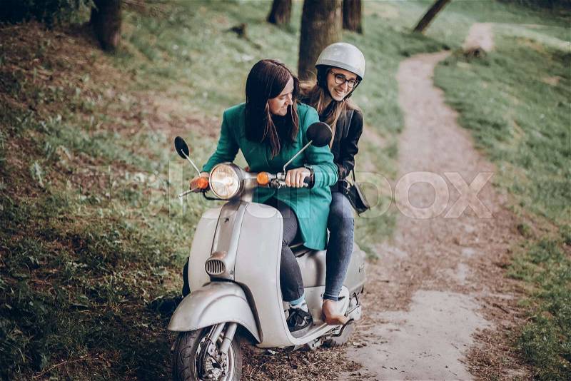 Couple of hipster girls riding a retro scooter in the wild, hipster woman on italian motorcycle in the park, stock photo