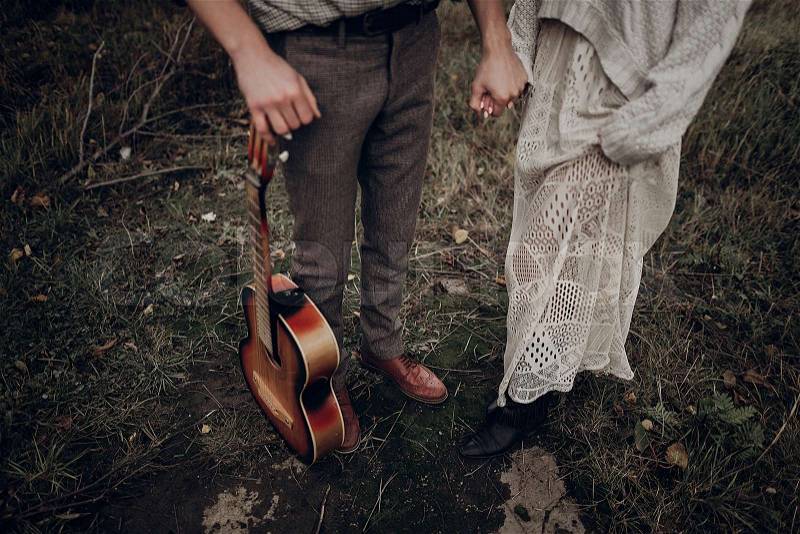Rustic wedding concept. boho gypsy woman and man with guitar posing in windy field. stylish hipster couple holding hands. atmospheric sensual moment. fashionable ..., stock photo