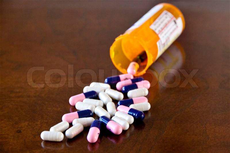 Prescription medicine pills pouring out of orange bottle on a table, stock photo