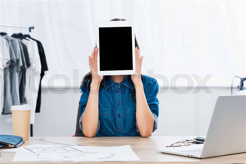 Young woman covering face by digital tablet with blank screen at working table , stock photo