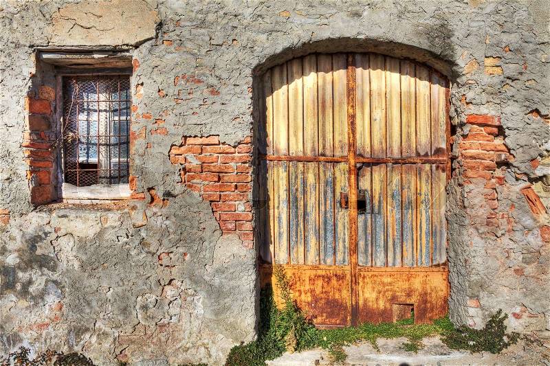 Old brick wall with metal rusty gate and small window in town of La Morra, Northern Italy, stock photo