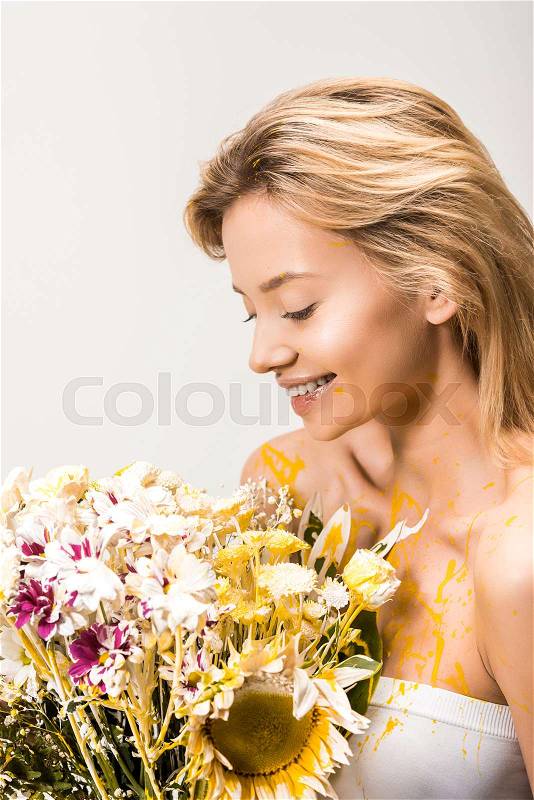 Smiling attractive woman with bouquet of flowers and yellow paint on body isolated on white, stock photo