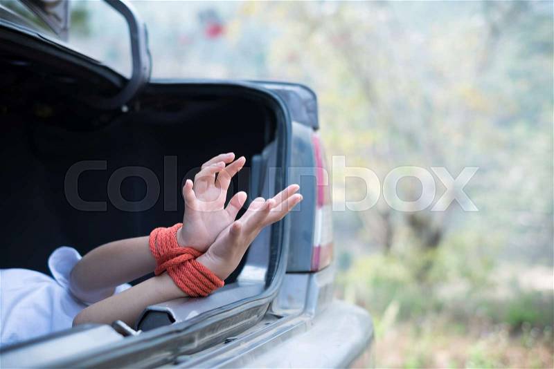 A girl with red rope tied hands lies in the trunk, stock photo