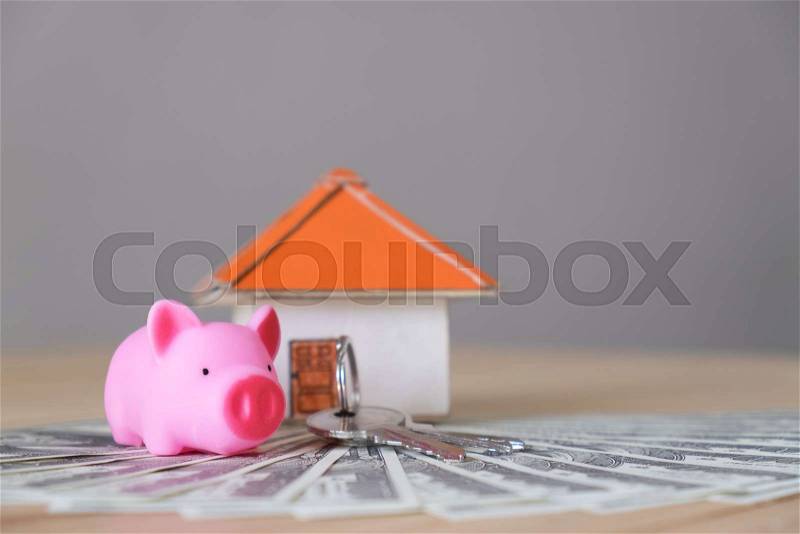 Pig money box and paper house with key on wooden wall background, stock photo