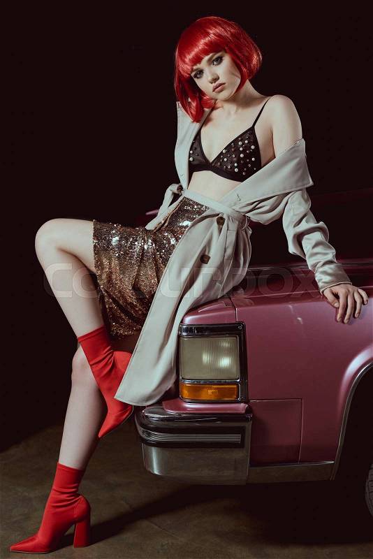 Full length view of beautiful girl in bra and trench coat sitting on car and looking at camera, stock photo