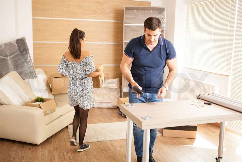 Smiling man putting together self assembly furniture in new home. Furniture in new house, stock photo