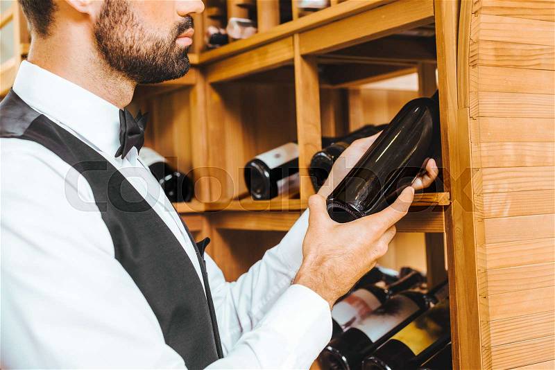 Cropped shot of young wine steward taking bottle from shelf at wine store, stock photo