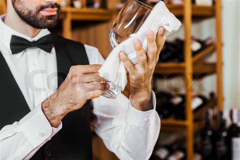 Cropped shot of young wine steward wiping glass at wine store, stock photo