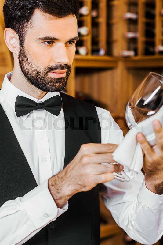 Handsome young wine steward wiping glass at wine store, stock photo