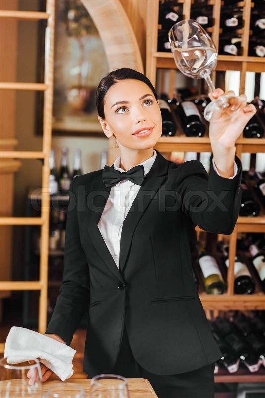 Beautiful female wine steward checking clear glass at wine store, stock photo