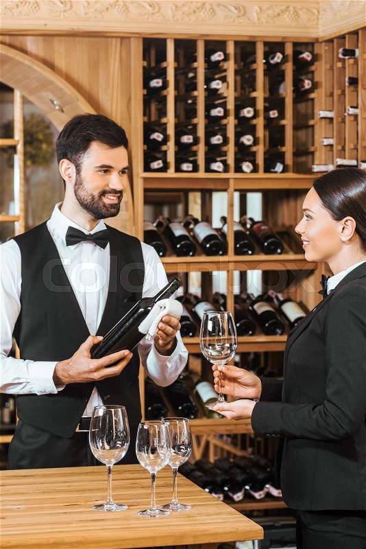 Couple of wine stewards pouring wine into glass for degustation at wine store, stock photo
