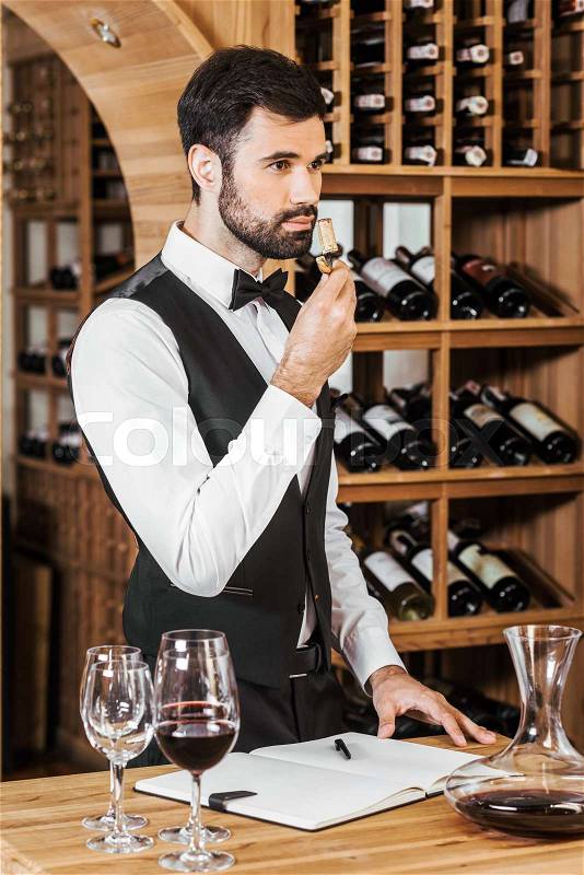 Handsome young wine steward examining aromatic bottle corc after opening wine at store, stock photo